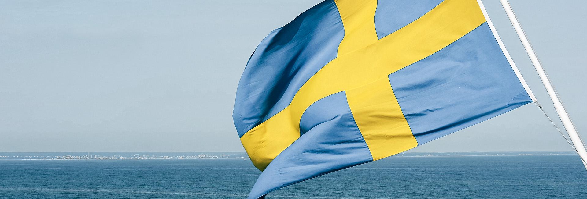 Svensk flagga som vajar i vinden med havet i bakgrunden